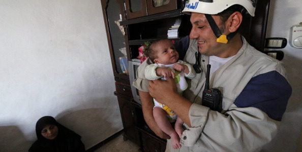Khaled (R), a member of Syria Civil Defence, kisses Syrian baby Mahmud Idilbi on July 12, 2014 in the Syrian city of Aleppo as Khaled has rescued the baby on June 18 from under the rubble of a building in the war-battered city. Mahmud Idlibi's dramatic rescue in the flashpoint northern city, a constant target of regime air raids, was shown in a video tweeted on July 11, 2014 by the team that saved him.  On the left is Mahmud's mother.  AFP PHOTO/AMC/ZEIN AL-RIFAI        (Photo credit should read ZEIN AL-RIFAI/AFP/Getty Images)